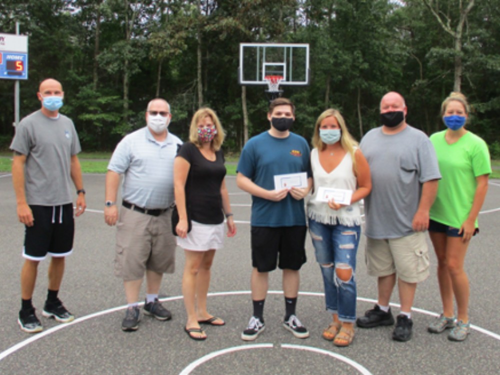 Group of adults in masks on outdoor basketball court holding up piece of paper