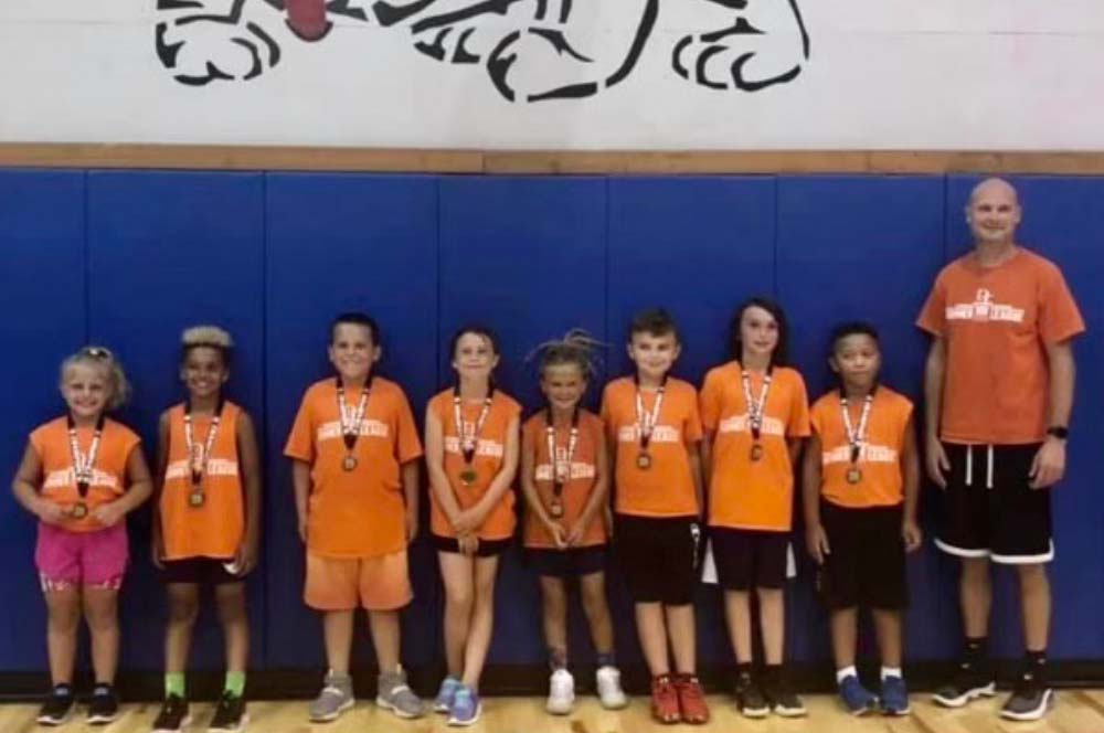 Youth basketball team in bright orange jerseys with medals in front of padded blue wall