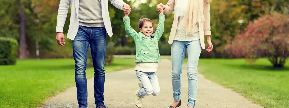 Parents swinging a smiling little girl as they walk.
